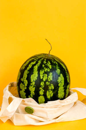 Watermelon in eco packaging on a yellow background. Detox in a reusable shopping bag. Zero waste healthy food delivery concept. Vertical position. Copy space.の写真素材