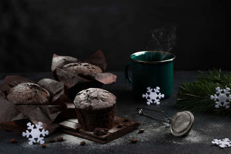 A festive evening with a warm drink and a chocolate muffin. green fir branches and snowflakes. Christmas time. Selective focus. Low key.の写真素材