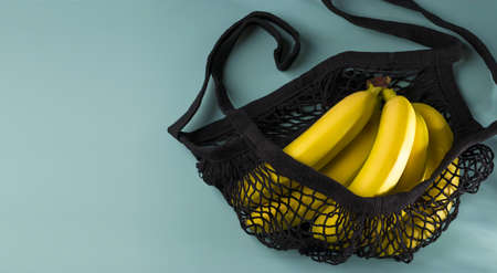 Yellow ripe bananas in a black eco-cotton string bag on a blue background. Reusable mesh shopping bag. Zero waste concept. Flat lay. Low key. View from above. Copy space.の写真素材