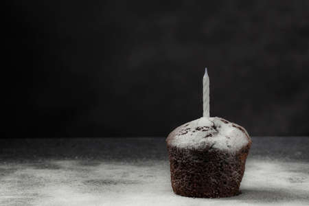 Delicious chocolate muffin with powdered sugar and white candle on a dark background. Birthday cake. Homemade baking. Festive concept. Low key. Copy space.の写真素材