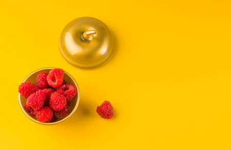 Ripe sweet raspberries in a bowl of golden color on a yellow background. Top view, high definition...