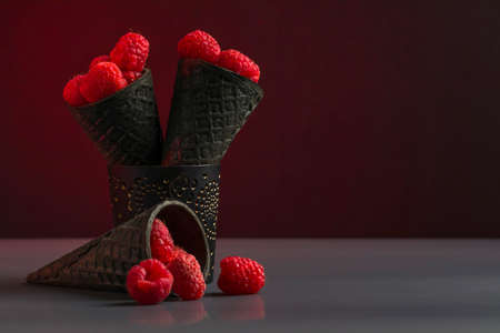 Red ripe sweet raspberries in waffle cones for ice cream on a dark background. Juicy healthy summer fruits. Low key. Copy spaceの写真素材