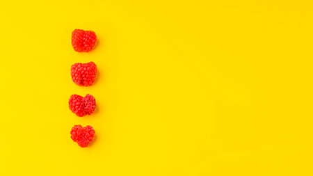 Delicious and juicy raspberries in the form of hearts on a yellow background. Minimalism for a designer. Summer, freshness and vegetarianism concept. Flat lay. Copy spaceの写真素材