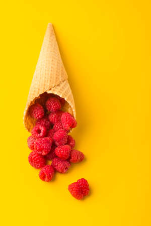 Minimalism. Raspberry explosion in a waffle cone on a yellow table. View from above. Healthy food...
