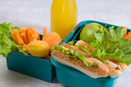 School food. Lunch box with a sandwich, fresh vegetables and fruits, a bottle of juice on a light...