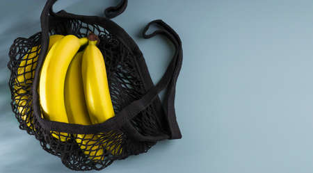 Zero waste concept. Yellow ripe bananas in a black eco-cotton string bag on a blue background. Reusable mesh shopping bag. Flat lay. Low key. View from above. Copy space.の写真素材