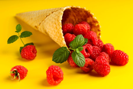 Raspberry explosion in ice cream waffle cone on yellow table. View from above. Healthy food concept. Minimalismの写真素材