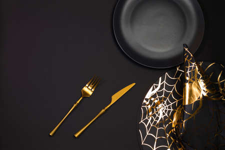 Halloween holiday. Serving on a dark table with a black pointed conical witch hat and black cutlery. Flat lay, top view trendy holiday concept. Copy spaceの写真素材