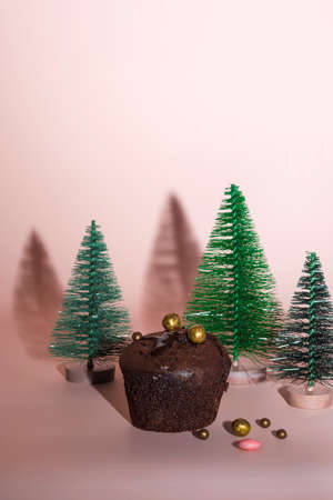 Christmas and New Year concept. Chocolate muffins, homemade cakes. Green Christmas trees on a pink gentle background. Hard shadows. Vertical positionの写真素材