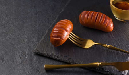 Hot grilled meat sausages on a slate board. Gold colored table knife and fork on a black background. Copy spaceの写真素材