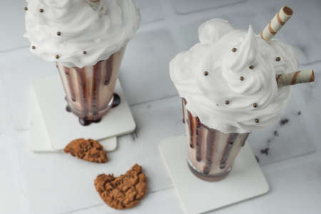 Close-up of chocolate milkshakes with whipped cream, with cookies in a tall glass on a light background. Delicious dessert drink. selective focusの写真素材