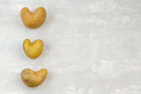 Some ugly heart-shaped potatoes on a gray background. Funny concept of vegetables or food waste. top view. copy spaceの写真素材