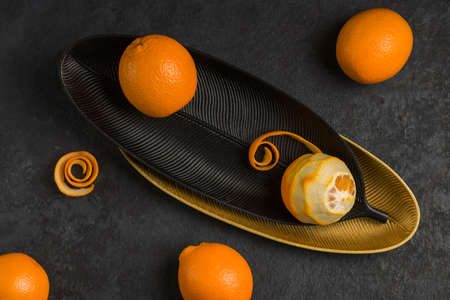 Several juicy oranges on black and gold plates against a dark background. The concept of healthy vegetarian food. top view. flat layの写真素材