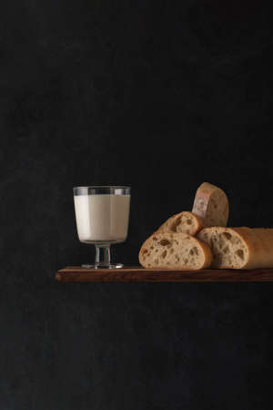 Milk in a glass cup, sliced freshly baked organic bread on a dark background. natural homemade food. copyspace.の写真素材
