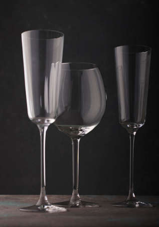 Tall glass goblets of different shapes for wine and champagne on a dark background. vertical...