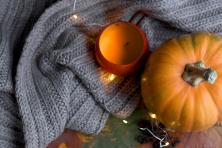 Autumn composition with orange pumpkin, leaves and gray knitted scarf plaid. The lights. Festive concept for Thanksgiving, Halloween. selective focus. top viewの写真素材