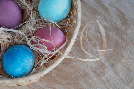 Spring holiday concept in eco style. Happy Easter. Bright colored eggs in a nutural basket with hay on a wooden cut natural background. Spring Easter concept in eco style. top view. copy spaceの写真素材
