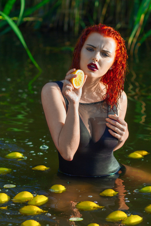 Beautiful european model with red hair sanding on the water with lemons aroundの写真素材