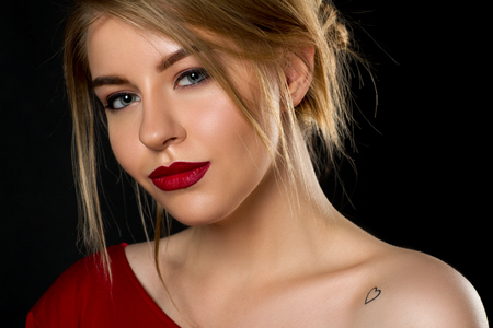 Beautiful blond girl in red dress and red lips in black backgroundの写真素材
