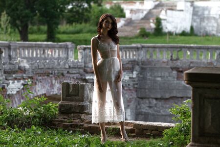 Elegant attractive slender young woman in a long white dress standing outdoors in front of a historical building with copy spaceの写真素材