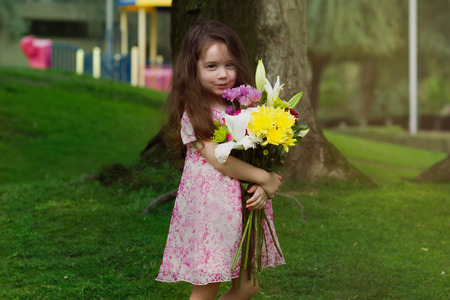 Closeup portrait of pretty serious funny girl kid holding flowers  outdoors summer backgroundの写真素材