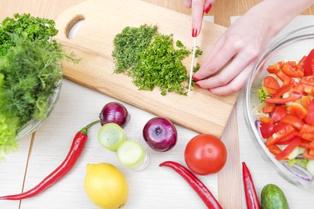 Women hands cut greens for a salad in the kitchen.