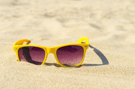 Yellow sunglasses in the sand on the beach closeup.の写真素材