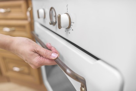 Female hand a little bit open to ventilate oven. Close-up.