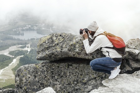 Woman photographer taking photo at mountain peak.の写真素材