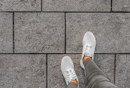 Legs in white sneakers on the street tiles.の写真素材