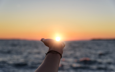 Hand reaches for the sun at sunset.