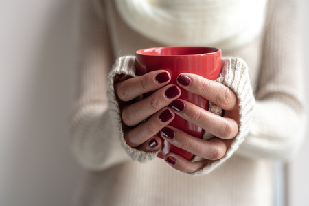 Young woman holds a cup with a hot drink in her hands.の写真素材