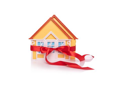 Toy house model bandaged with a red ribbon on white background.の写真素材