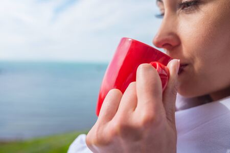 Girl wrapped in a blanket on the balcony in the morning drinks coffee or tea.