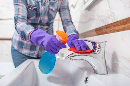 Cleaning in the bathroom. A woman wipes the sink and washbasin faucet.の写真素材