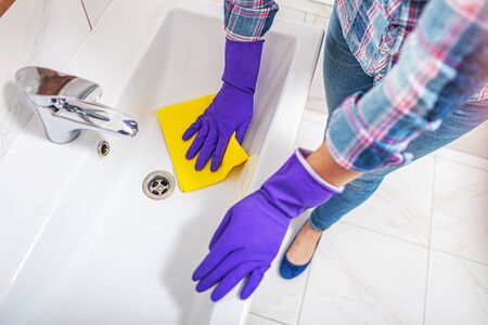 Cleaning in the bathroom. A woman wipes the sink and washbasin faucet.の写真素材