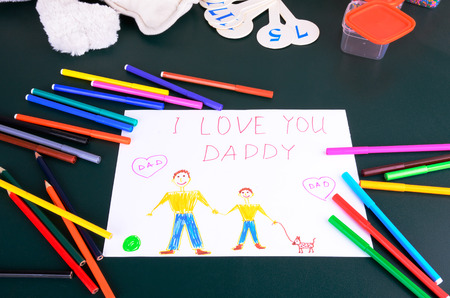 child's drawing "Daddy, I love you" and a lot of colored pencils, markers and toy on the green tableの写真素材
