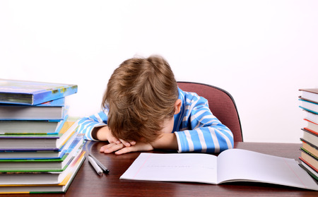 little boy laid his head on the desk on the light background, horizontalの写真素材