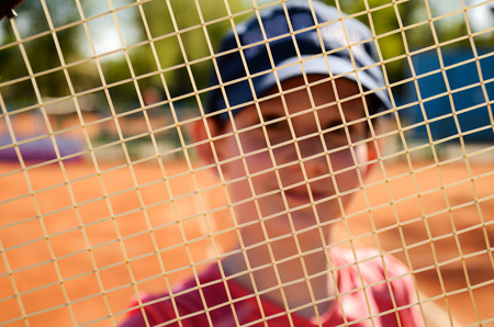 smiling teenage girl looking through the net of a tennis racket string  front view  focus on the stringsの写真素材
