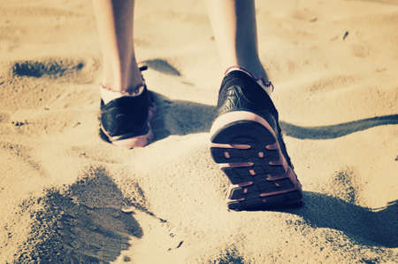 girl feet in sneakers go away on the sand. tinted, horizontalの写真素材