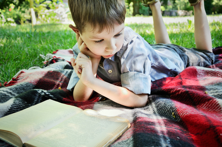 little boy reading a book while lying on a mat in the park close up horizontalの写真素材
