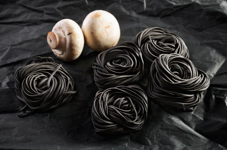 five servings of black pasta with cuttlefish ink and two mushroom on a dark background. close-up. horizontal formatの写真素材