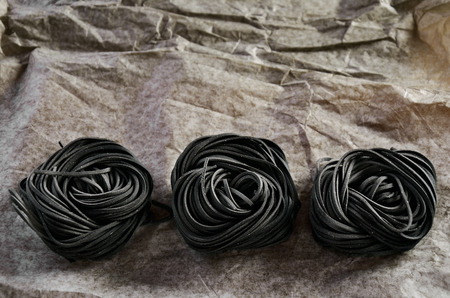 three servings of pasta with black cuttlefish ink on a paper background. horizontalの写真素材