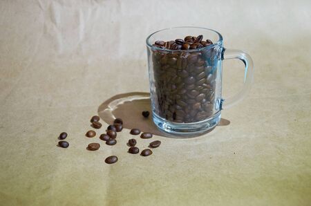 roasted coffee beans are placed in and around a clear glass Cup on a brown backgroundの写真素材