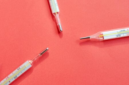 three medical thermometers lie on a red background