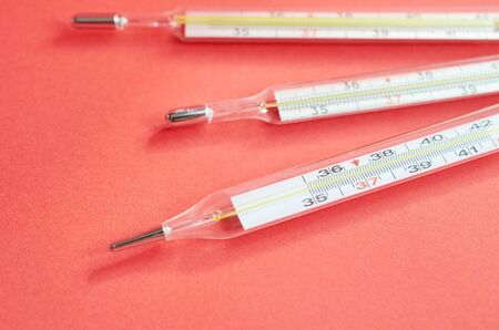 three medical thermometers lie on a red background