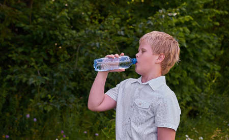A boy drinks water from a plastic bottle on a walk in the Park in summer