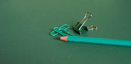A simple pencil and paper clips lie on a simple green background. Close-up, macro