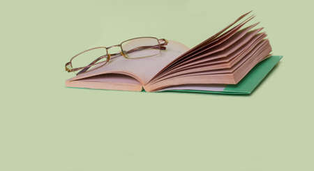 The glasses are lying on an open book on a solid green backgroundの写真素材
