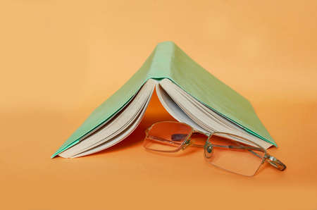 The glasses are next to the book on a uniform orange backgroundの写真素材